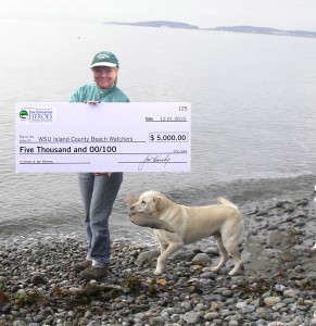 Image of Jan Holmes on beach with huge check from Cox Conserves