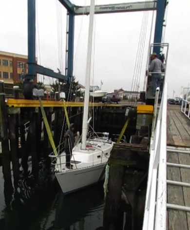 Image of sailboat being lowered into the the water via travel lift. AKA splash