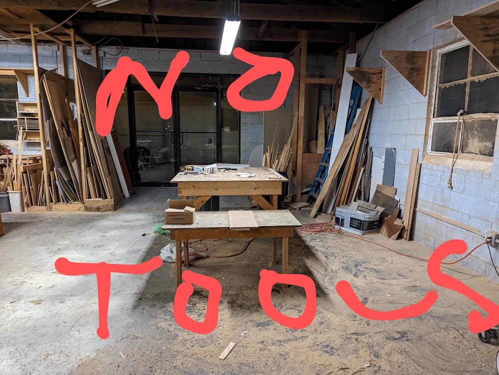 A wood shop with work benches. Red writing says No Tools.