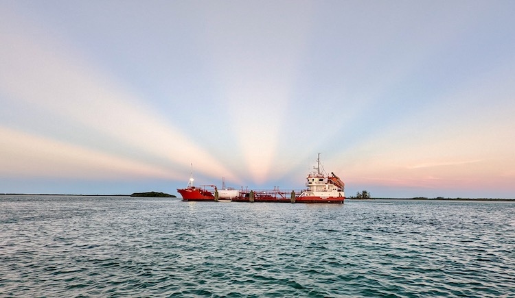 red fuel tanker in Bimini at sunset with blue sky and pink sun rays in the background.