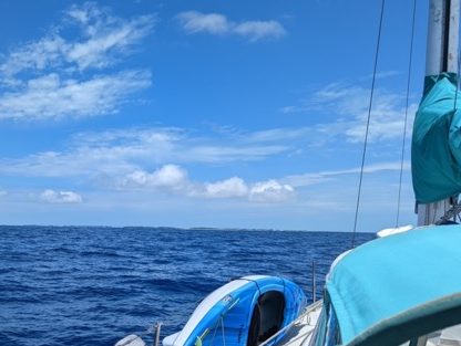 land ho! a low island on the horizon of a blue sea.