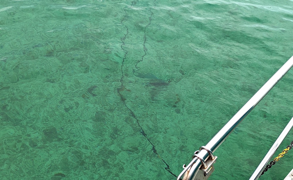 Anchor chain and anchor lying on the bottom seen through clear, turquoise water.