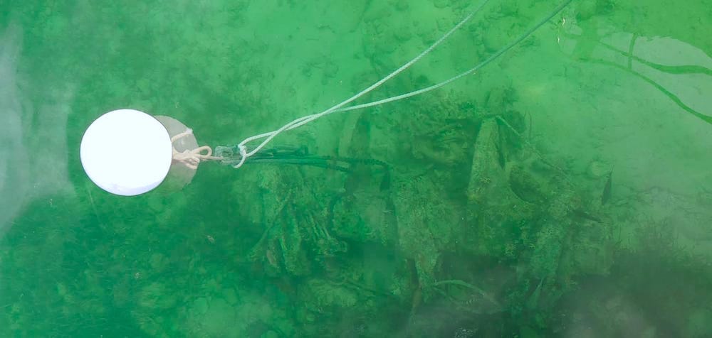 Birds eye view of a white mooring ball attached to underwater wrecked heavy machinery.
